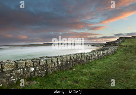 Blick nach Osten, entlang Cawfield Klippen, Hadrianswall, Northumberland - eine Morgendämmerung mit tiefliegenden Nebel auf den Feldern anzeigen Stockfoto