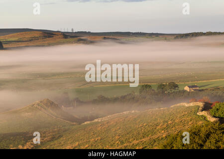 Blick nach Westen, entlang Cawfield Klippen, Hadrianswall, Northumberland - eine Morgendämmerung mit tiefliegenden Nebel auf den Feldern anzeigen Stockfoto