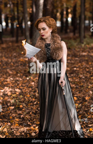 Junge, attraktive Frau im Herbst Park stehen und blickte brennen Noten in ihrer Hand, stützte sich auf Zuckerrohr. Stockfoto