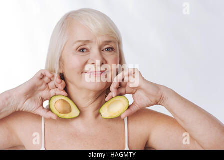 Optimistische gealterte Frau, die Avocado Hälften in ihren Händen Stockfoto