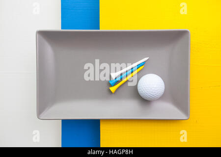 Graue Keramik Teller mit Golf-Ausrüstungen auf über weißen, blauen und gelben Holztisch, Rechteck Schale Stockfoto