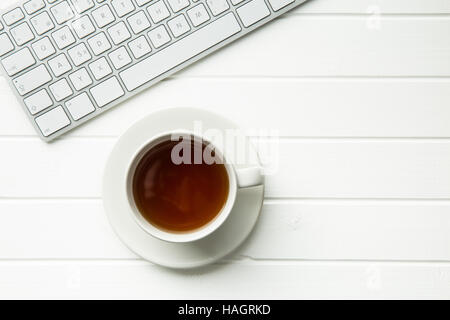 Tasse Tee und Computer-Tastatur auf weißen Tisch. Ansicht von oben. Stockfoto