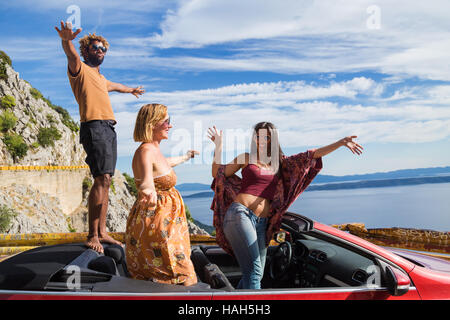 Gruppe der glückliche junge Menschen in das rote Cabrio Auto stehen und winken. Stockfoto