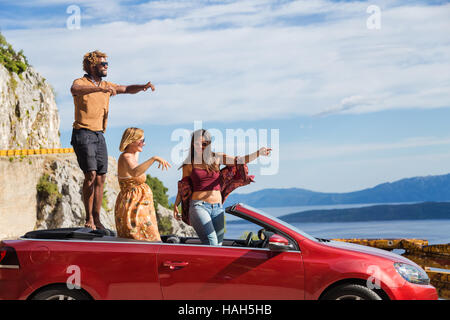 Gruppe der glückliche junge Menschen in das rote Cabrio Auto stehen und winken. Stockfoto