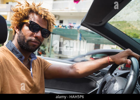 Junge schwarze Mann mit Dread Locks mit Sonnenbrille im Cabrio Auto zu sitzen. Stockfoto