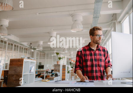Schuss der junge Geschäftsmann in Freizeitkleidung auf moderne Start-up Unternehmen Büroräume, auf Desktop-Computer arbeiten. Stockfoto