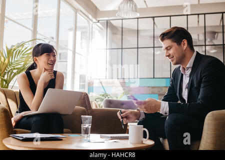 Aufnahme von zwei professionelle Geschäftstreffen in Lobby des modernen Büros. Frau mit Mann mit Handy am Laptop arbeiten. Stockfoto