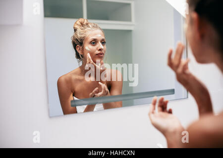 Schöne junge Frau auftragen Creme im Badezimmer. Weibliche Blick in den Spiegel und aufsetzen Gesichtscreme. Stockfoto