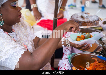 SALVADOR, Brasilien - 2. Februar 2016: Brasilianische Baiana Frau montiert einen Teller mit traditionellen Acaraje Krapfen aus einem Stall. Stockfoto