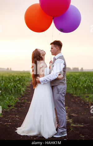 Brautpaar stehend auf das Feld mit großen hellen bunten Luftballons, Ganzkörper Stockfoto