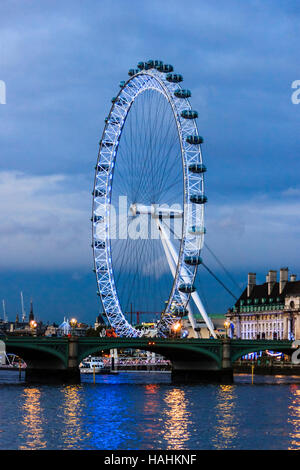Das London Eye ist abends beleuchtet, aus über die Themse auf der Victoria Embankment, London, UK gesehen Stockfoto