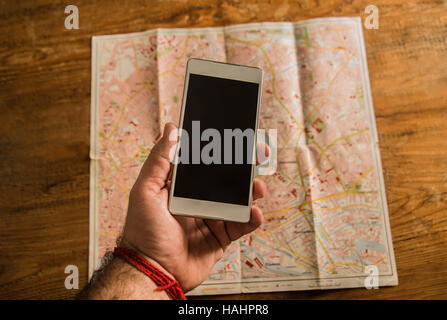 Hand halten Handys mit Unschärfe Perspektive Fahrplan Hintergrund. Vintage Karte liegen auf Holztisch Stockfoto