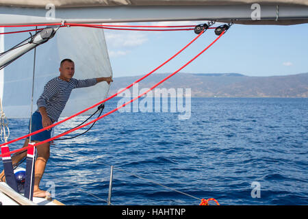 Junger Mann in der Nähe die Segel auf dem Boot. Setzen das Gerät auf einem Segelschiff während Meer Regatta. Stockfoto