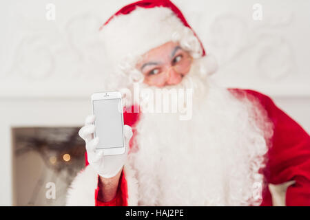 Santa Claus zeigt eine Smartphone gegen Kamin Stockfoto
