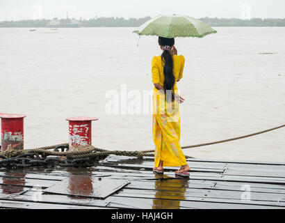 Junge burmesische Frau in traditioneller Kleidung beobachtete den Yangon Fluss vom Botahtaung Steg an einem regnerischen Tag. Stockfoto