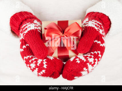 Weibliche Hände halten Weihnachtsgeschenk in rote Handschuhe Stockfoto