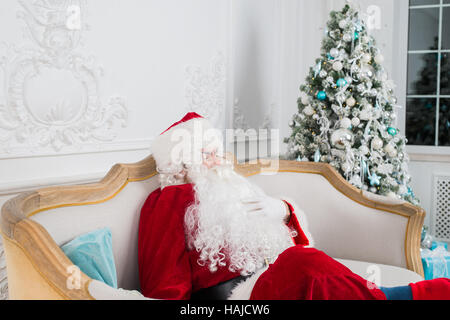 Santa Claus auf Sofa gegen Weihnachtsbaum zu Hause entspannen Stockfoto