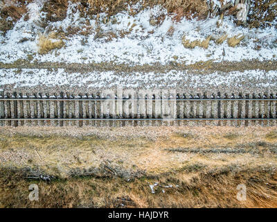Luftaufnahme der einzelnen Railroad tracks auf der Rückseite Land mit einigen Unkraut und Schnee Stockfoto