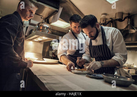 Joni Francisco, Chef de Partie, bereitet eine Gericht, während Tom Brown, Senior Souschef und ein Kellner auf, während mittags im Restaurant. Die Stockfoto