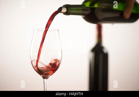 Gießen Rotwein in Weinglas aus grünen Flasche, weißer Hintergrund Stockfoto