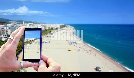 Blick auf dem Handy-Display während der Aufnahme eines Costa Brava Strand von Calella, Spanien. Das Mobiltelefon in Händen hält und unter einer phot Stockfoto