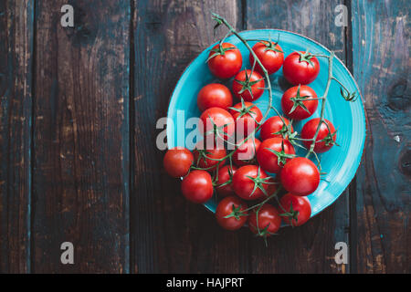 Cherry-Tomaten am Rebstock. Blaue Teller mit Cherry-Tomaten auf Holztisch. Stockfoto