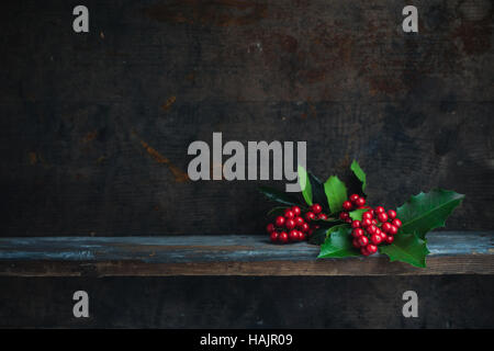 Christmas Holly Zweig. Weihnachts-Dekoration mit roten Beeren auf ein Holzbrett gelegt. Stockfoto