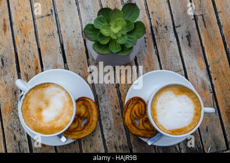 Zwei Tassen Kaffee auf einem Holztisch im Freien mit dänischen Keksen und Löffel Barrista. Stockfoto