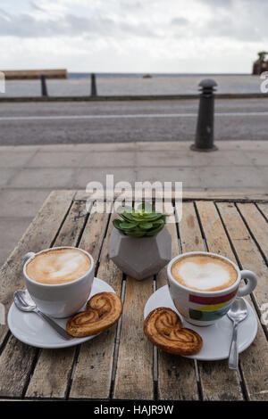 Zwei Tassen Kaffee auf einem Holztisch im Freien mit dänischen Keksen und Löffel Barrista. Stockfoto