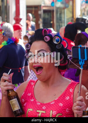 Britische Straße Kostümfest in Benidorm, Spanien. Junge Frau trägt Rollen im Haar mit Bierflasche in der hand. Stockfoto