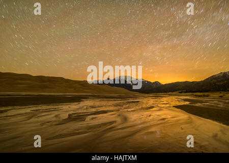 Spring Night am Great Sand Dunes National Park - Langzeitbelichtung fängt Sternspuren im Nachthimmel über Frühling Medano Creek. Stockfoto