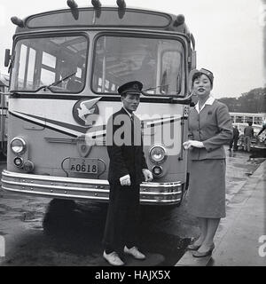 1950er Jahre, historisch, Tokio, Japan, uniformierte männliche und weibliche Reiseleiter stehen vor einem geparkten Isuzu Touristenbus in einer nassen Straße und warten auf ihre Passagiere. Stockfoto