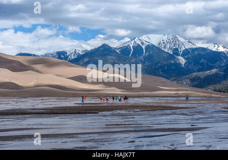 Frühling am Medano Creek - eine Gruppe, die Kinder in Medano Creek am Fuße der großen Sanddünen und schneebedeckten Gipfeln spielen. Stockfoto