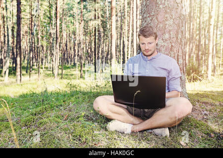 junger Mann mit seinem Laptop im Freien in der Natur arbeiten Stockfoto