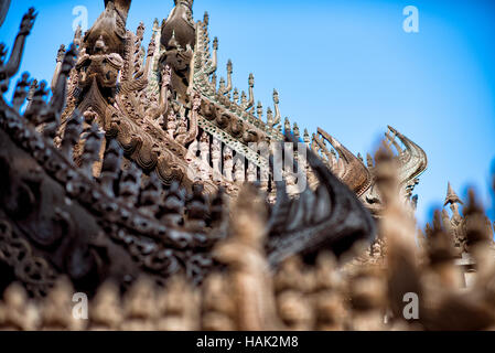 Shwenandaw Kloster Holzschnitzereien Mandalay Myanmar // MANDALAY, Myanmar – aufwändig geschnitzte Holzfiguren säumen die Dachlinie und das Geländer des Shwenandaw Klosters (auch bekannt als Shwe Nandaw Kyaung) und zeigen traditionelle buddhistische architektonische Kunstfertigkeit von Birma. Das Kloster wurde 1878 aus Teakholz erbaut und ist das einzige erhaltene originale Holzgebäude aus dem Königspalast Mandalay. Das Gebäude war ursprünglich König Mindon Mindons private königliche Wohnung, wo er 1878 starb, und dann von König Thibaw Min innerhalb von 31 Tagen nach dem Tod seines Vaters in ein buddhistisches Kloster umgewandelt. Das Kloster Stockfoto