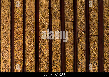 MANDALAY Myanmar // MANDALAY, Myanmar — aufwendig geschnitzte Teakplatten zeigen traditionelle buddhistische Motive, die in Blattgold auf dunkelrotem Hintergrund im Shwenandaw Kloster (auch bekannt als Shwe Nandaw Kyaung) gemalt sind. Das 1878 erbaute Kloster stellt das einzige erhaltene originale Holzgebäude aus dem Mandalay Royal Palace Komplex dar und war ursprünglich König Mindon Mindons private königliche Wohnung, wo er 1878 starb. Das Gebäude wurde vollständig aus Teakholz mit traditionellen Einsteckschlössern und Zapfenschreinereien ohne Nägel gebaut und verfügt über umfangreiche Holzschnitzereien Stockfoto