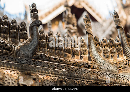 Holzschnitzereien Mandalay Myanmar // MANDALAY, Myanmar — aufwändig geschnitzte Holzfiguren säumen das Geländer des Shwenandaw Klosters (auch bekannt als Shwe Nandaw Kyaung), der einzigen erhaltenen ursprünglichen Struktur aus dem Mandalay Royal Palace Komplex. Das 1878 aus Teakholz erbaute Kloster war ursprünglich König Mindon Mindon Minds private königliche Wohnung, wo er 1878 starb. König Thibaw Min baute das Gebäude innerhalb von Tagen nach dem Tod seines Vaters in ein buddhistisches Kloster um und verlegte es an seinen heutigen Standort in der Nähe des Mandalay Hill. Die Brandung des Klosters Stockfoto