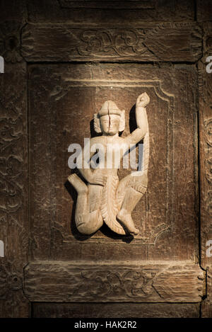 MANDALAY Myanmar // MANDALAY, Myanmar — Eine tanzende Figur, die in die Dekoration einer der Türverkleidungen des Shwenandaw Klosters (auch bekannt als Shwe Nandaw Kyaung) geschnitzt wurde, der einzigen erhaltenen ursprünglichen Holzkonstruktion aus dem Königspalast von Mandalay. Das 1878 aus geschnitztem Teakholz erbaute Kloster war ursprünglich König Mindon Mindons private königliche Wohnung, wo er 1878 starb, und dann von König Thibaw Min in ein buddhistisches Kloster umgewandelt. Das Gebäude war ursprünglich Teil des Königspalastes in Amarapura, bevor es von Elefanten nach Manda transportiert wurde Stockfoto