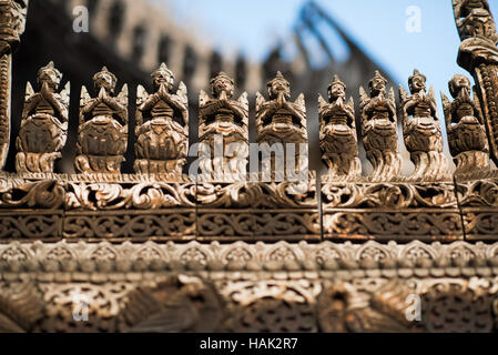 Shwenandaw Kloster Holzschnitzereien Mandalay Myanmar // MANDALAY, Myanmar – aufwändig geschnitzte Holzfiguren säumen die Dachlinie und das Geländer des Shwenandaw Klosters (auch bekannt als Shwe Nandaw Kyaung) und zeigen traditionelle buddhistische architektonische Kunstfertigkeit von Birma. Das Kloster wurde 1878 aus Teakholz erbaut und ist das einzige erhaltene originale Holzgebäude aus dem Königspalast Mandalay. Das Gebäude war ursprünglich König Mindon Mindons private königliche Wohnung, wo er 1878 starb, und dann von König Thibaw Min innerhalb von 31 Tagen nach dem Tod seines Vaters in ein buddhistisches Kloster umgewandelt. Das Kloster Stockfoto