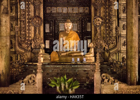 MANDALAY Myanmar // MANDALAY, Myanmar – Eine goldene Buddha-Statue mit Safrangürtel befindet sich in einem aufwändig geschnitzten Holzschrein im Shwenandaw Kloster (auch bekannt als Shwe Nandaw Kyaung). Das Kloster wurde 1878 aus Teakholz unter Verwendung traditioneller Einsteckschlösser und Tenonschreinerei errichtet und diente ursprünglich als königliche Privatwohnung von König Mindon Min, wo er 1878 starb. König Thibaw Min baute das Gebäude innerhalb von Tagen nach dem Tod seines Vaters in ein buddhistisches Kloster um und verlegte es vom Königspalast Mandalay an seinen heutigen Standort in der Nähe von Mand Stockfoto