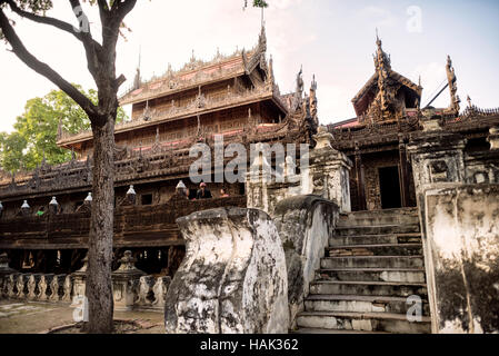 Shwenandaw Kloster Holzschnitzereien Mandalay Myanmar // MANDALAY, Myanmar – Betontreppen führen zum Shwenandaw Kloster (auch bekannt als Shwe Nandaw Kyaung), einem Teakholz-Gebäude, das für seine komplizierten Holzschnitzereien bekannt ist, die buddhistische Mythologie darstellen. Das 1878 erbaute Kloster war ursprünglich König Mindon Mindons private königliche Wohnung im Mandalay Palace Komplex, bevor es nach dem Tod des Königs in ein buddhistisches Kloster umgewandelt wurde. Das Gebäude stellt die einzige erhaltene ursprüngliche Holzkonstruktion aus dem Königspalast von Mandalay dar und wurde vollständig aus Teakholz mit traditioneller Mortis gebaut Stockfoto