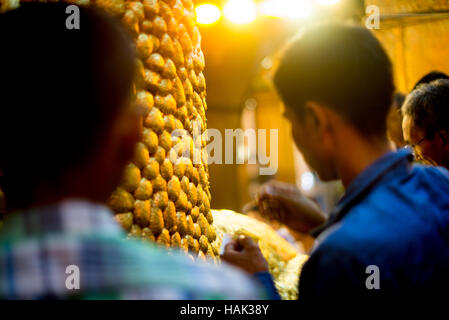 Mahamuni Buddha Bild Gold Blatt Anwendung Mandalay Myanmar // MANDALAY, Myanmar — Männer wenden Blattgold auf das Mahamuni Buddha Bild im inneren Heiligtum des Mahamuni Buddha Tempels an (auch bekannt als Mahamuni Pagoda). Die Bronzestatue mit einem Gewicht von 6,5 Tonnen und einer Höhe von 3,82 Metern gilt als eine von nur fünf originalen Gestalten Buddhas, die zu seinen Lebzeiten entstanden sind. Im Laufe der Jahrhunderte haben Gläubige etwa 15 Zentimeter Blattgold auf das Bild aufgetragen, wobei nur männliche Anbeter die Statue direkt berühren und vergolden dürfen. Der 1785 von König Bodawpaya erbaute Tempel beherbergt das Stockfoto