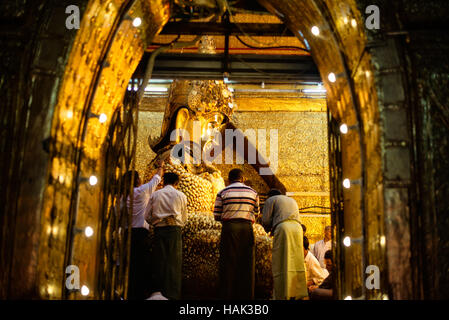 Mahamuni Buddha Image Gold Leaf Mandalay Myanmar // MANDALAY, Myanmar — die Menschen tragen Blattgold auf das verehrte Mahamuni Buddha-Bild am Mahamuni Buddha Tempel (auch bekannt als Mahamuni Pagode). Die Bronzestatue mit einem Gewicht von 6,5 Tonnen und einer Höhe von 3,82 Metern gilt als eine von nur fünf originalen Gestalten Buddhas, die zu seinen Lebzeiten entstanden sind. Der Tempel wurde 1785 von König Bodawpaya erbaut und beherbergt das Bild aus dem alten Arakan-Königreich. Im Laufe der Jahrhunderte haben die Gläubigen etwa 15 Zentimeter Blattgold auf die Statue aufgetragen. Nur Männer sind erlaubt Stockfoto