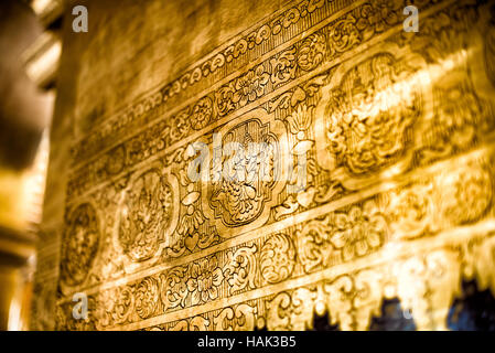 Mahamuni Buddha-Tempel verzierte goldene Schnitzereien Mandalay Myanmar / MANDALAY, Myanmar – komplizierte vergoldete Reliefs von Himmelsfiguren und Blumenmotive schmücken den Mahamuni Buddha-Tempel. König Bodawpaya beauftragte den Komplex 1785, einen 14,3 Tonnen (6,5 Tonnen) Bronze-Buddha zu verwahren, von dem angenommen wird, dass er eine von fünf Gleichnissen zu Lebzeiten des religiösen Gründers ist. Das schwere Blattgold dieser traditionellen burmesischen Schnitzereien spiegelt die Hingabe am Hauptaltar wider, wo Jahrhunderte von Pilgern eine 15 cm große Goldschicht auf die zentrale Statue aufgetragen haben. Stockfoto