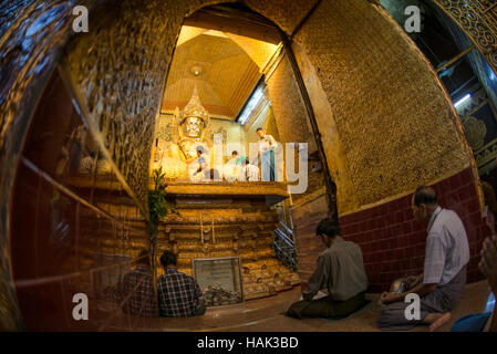 Mahamuni Buddha Bild Gold Blatt Anwendung Mandalay Myanmar // MANDALAY, Myanmar — Gläubige und Pilger treffen sich in der äußeren Halle des Mahamuni Buddha Tempels (auch bekannt als Mahamuni Pagoda), um den Prozess der Anwendung von Blattgold auf dem verehrten Mahamuni Buddha Bild zu beobachten. Der Tempel hat traditionelle Geschlechterbeschränkungen, wonach nur Männer das innere Heiligtum betreten und direkt an der Anwendung von Blattgold auf die Bronzestatue teilnehmen dürfen, die 6,5 Tonnen wiegt und mit etwa 15 Zentimeter Blattgold aus Jahrhunderten von Andachtsopfern bedeckt ist. Frauen und Othe Stockfoto