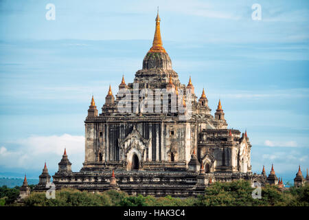Thatbyinnyu-Tempel Bagan Myanmar Blauer Himmel | BAGAN, Myanmar — Der Thatbyinnyu-Tempel erhebt sich klar vor einem offenen Himmel, seine zwei gestapelten würfelförmigen Stockwerke und die sich verjüngende Sikhara ragen etwa 201 bis 210 Fuß (61 bis 64 m) über die Ebene. Der Name leitet sich vom Pali Sabbannu ab, „der Allwissende“, ein Epitheton des Buddha, was dieselbe devotional Logik widerspiegelt, die das Hauptbild nicht im zugänglichen Erdgeschoss, sondern hoch im oberen Stockwerk platzierte. Stockfoto
