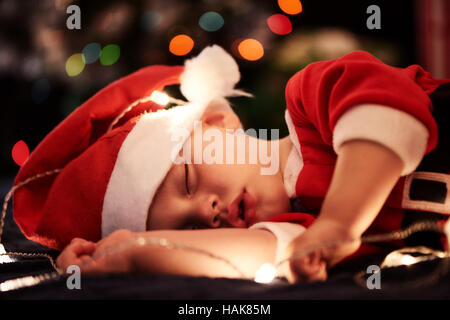 Baby schläft in Santa Outfit für die Weihnachtszeit in der Nähe von Baum Stockfoto