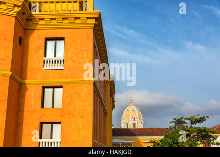 Orange Gebäude im Kolonialstil in Cartagena/Kolumbien mit der Kuppel der Kirche San Pedro Claver im Hintergrund Stockfoto