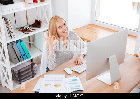 Glücklich lächelnd Geschäftsfrau Ordnung Anzeichen beim Sitzen an ihrem Arbeitsplatz Stockfoto