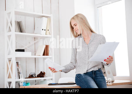 Junge casual Geschäftsfrau hält Dokumente und sitzt auf dem Schreibtisch Stockfoto